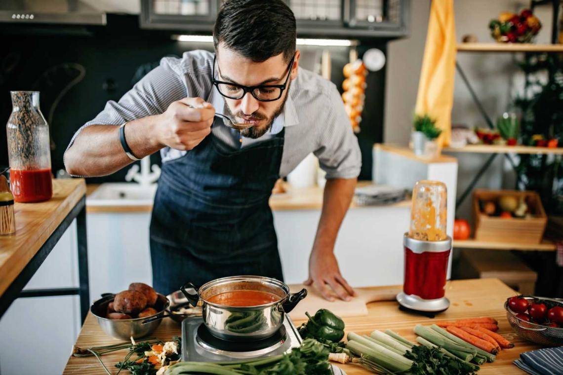 man in apron tasting food from a spoon